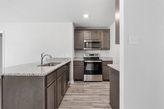 kitchen with light stone counters, sink, kitchen peninsula, stainless steel appliances, and light wood-type flooring