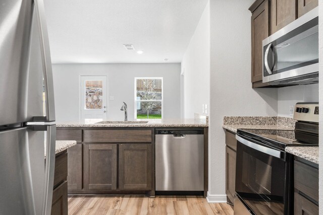 kitchen featuring light hardwood / wood-style floors, dark brown cabinetry, light stone counters, sink, and appliances with stainless steel finishes