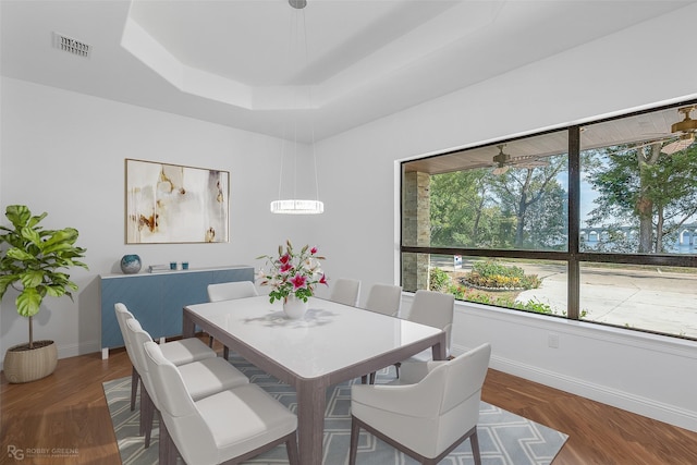 dining room with dark hardwood / wood-style floors, ceiling fan, and a raised ceiling