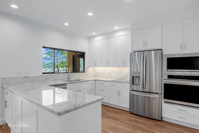 kitchen featuring light stone countertops, kitchen peninsula, stainless steel appliances, sink, and white cabinetry