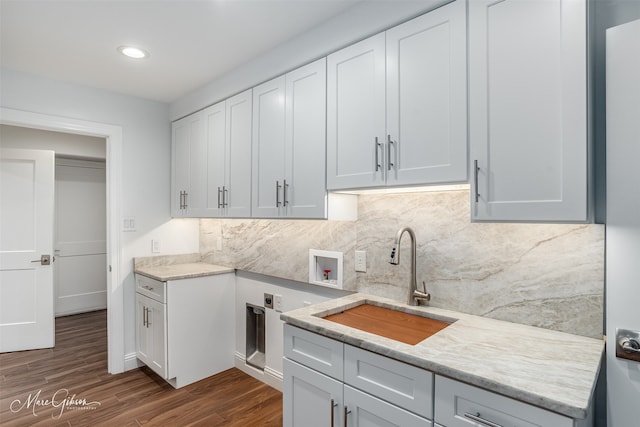 kitchen with sink, decorative backsplash, light stone countertops, dark hardwood / wood-style flooring, and white cabinetry