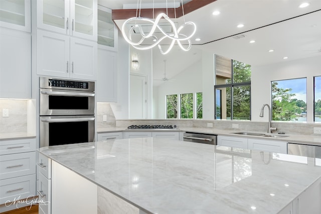 kitchen with white cabinets, sink, decorative light fixtures, light stone counters, and stainless steel appliances