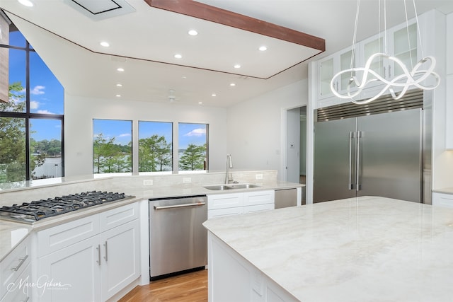 kitchen featuring white cabinetry, sink, light stone counters, pendant lighting, and appliances with stainless steel finishes