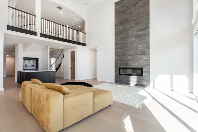 living room featuring a tile fireplace, a towering ceiling, and light wood-type flooring