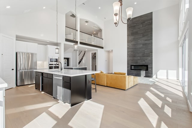 kitchen featuring appliances with stainless steel finishes, high vaulted ceiling, a large fireplace, a center island with sink, and pendant lighting