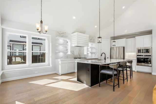 kitchen featuring sink, tasteful backsplash, light wood-type flooring, stainless steel appliances, and an island with sink