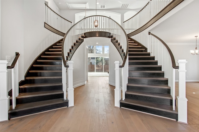 stairway with ornamental molding, an inviting chandelier, wood-type flooring, and a towering ceiling