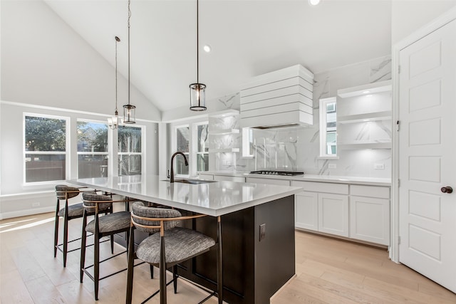 kitchen featuring decorative light fixtures, backsplash, custom range hood, sink, and a center island with sink