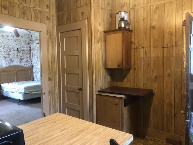 kitchen featuring ceiling fan, wooden walls, and dark carpet