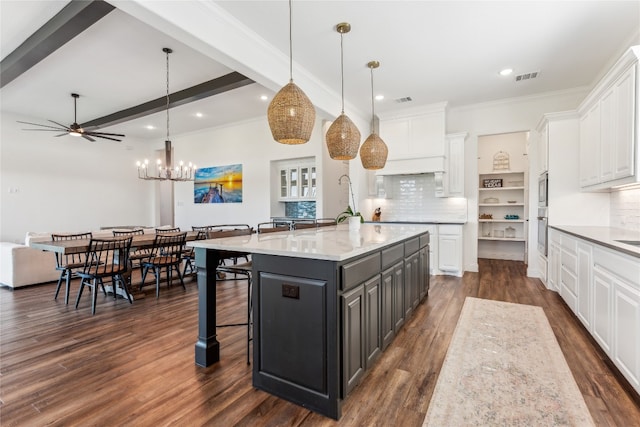 kitchen with tasteful backsplash, dark wood-type flooring, a kitchen island with sink, white cabinets, and pendant lighting