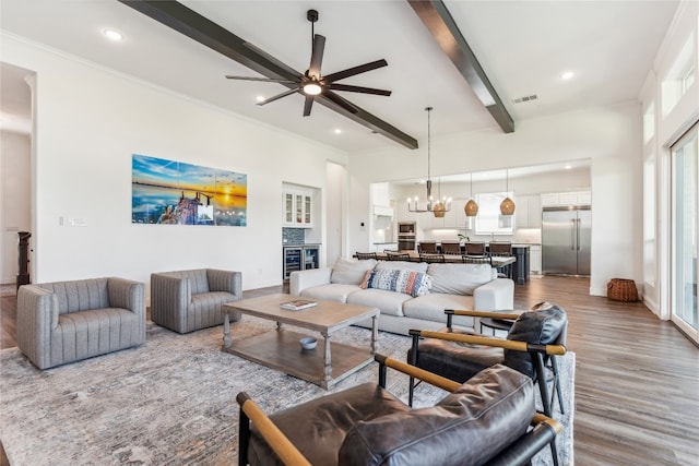 living room with ceiling fan with notable chandelier, beamed ceiling, and hardwood / wood-style floors