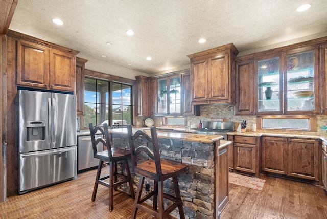 kitchen with a breakfast bar, light stone counters, appliances with stainless steel finishes, a kitchen island, and backsplash