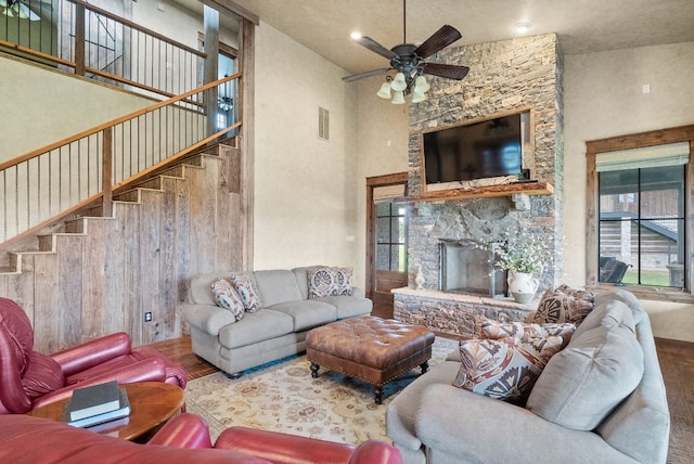 living room featuring a stone fireplace, wood-type flooring, ceiling fan, and a high ceiling