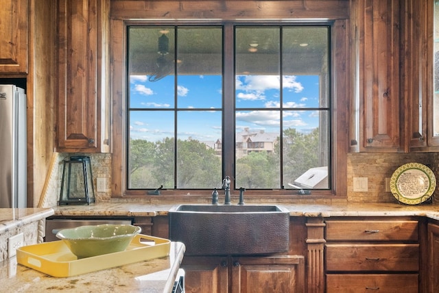 kitchen with light stone counters, sink, tasteful backsplash, and stainless steel refrigerator