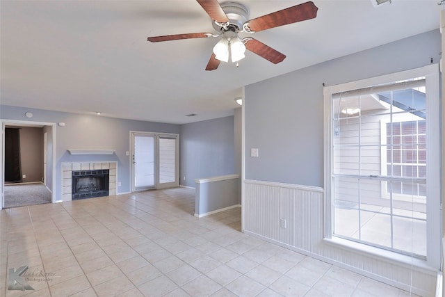 unfurnished living room featuring ceiling fan, a tile fireplace, and light tile floors