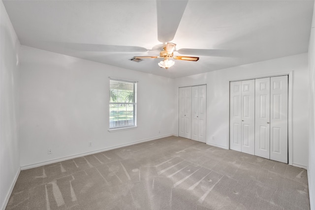 unfurnished bedroom featuring multiple closets, light colored carpet, and ceiling fan