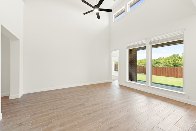 unfurnished living room with a high ceiling, ceiling fan, and light hardwood / wood-style flooring