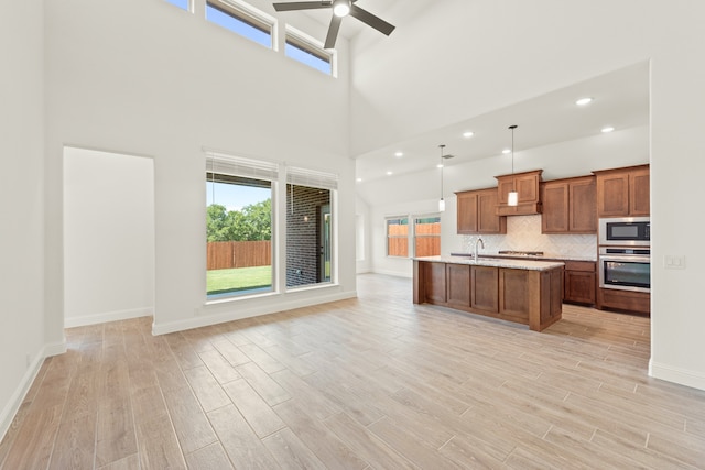 kitchen with pendant lighting, light wood-type flooring, stainless steel appliances, a towering ceiling, and a center island with sink