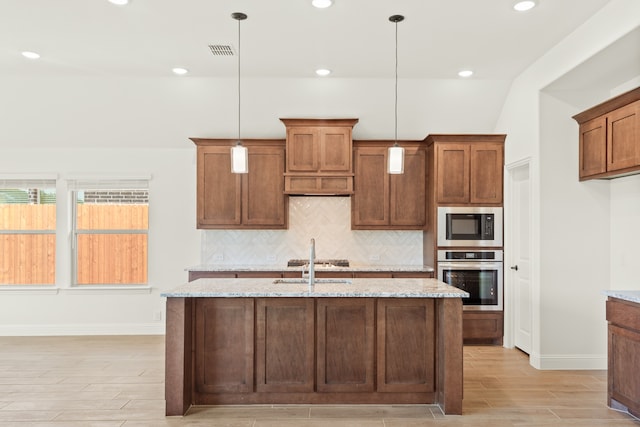 kitchen featuring light stone counters, pendant lighting, a center island with sink, and appliances with stainless steel finishes