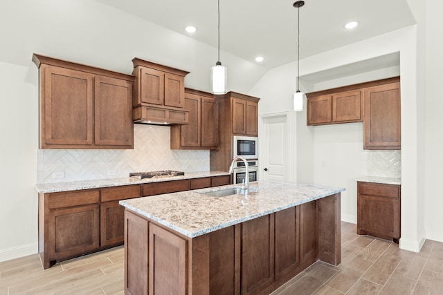 kitchen with sink, an island with sink, lofted ceiling, decorative light fixtures, and light stone countertops