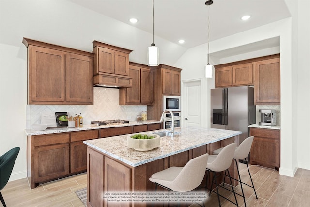 kitchen featuring appliances with stainless steel finishes, hanging light fixtures, light stone counters, lofted ceiling, and a center island with sink