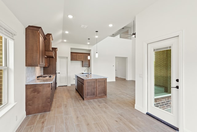 kitchen with pendant lighting, light stone counters, light hardwood / wood-style flooring, and sink