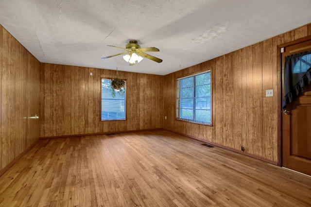 unfurnished room with ceiling fan, a textured ceiling, light hardwood / wood-style floors, and wood walls