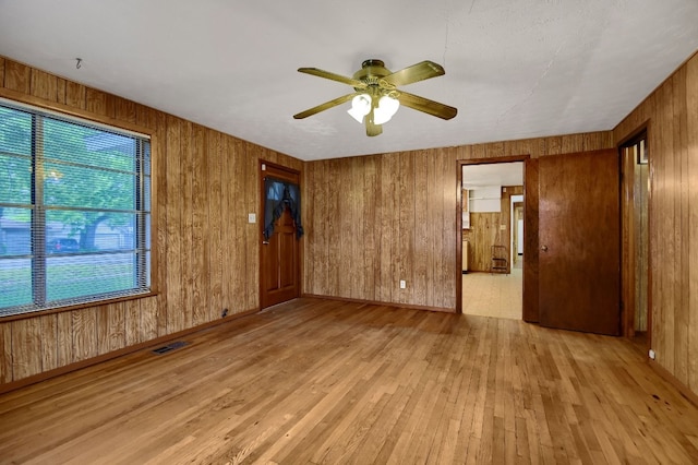 empty room featuring wooden walls, light wood-type flooring, and ceiling fan