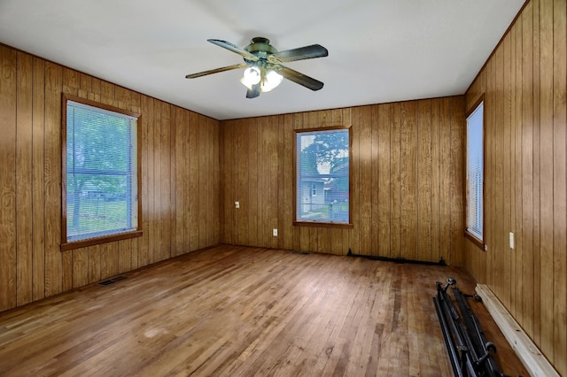 unfurnished room featuring ceiling fan, light hardwood / wood-style floors, and wood walls