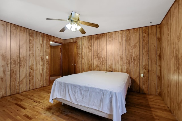 bedroom with wood walls, hardwood / wood-style flooring, and ceiling fan