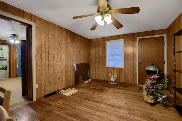 interior space featuring light hardwood / wood-style flooring, wooden walls, and ceiling fan