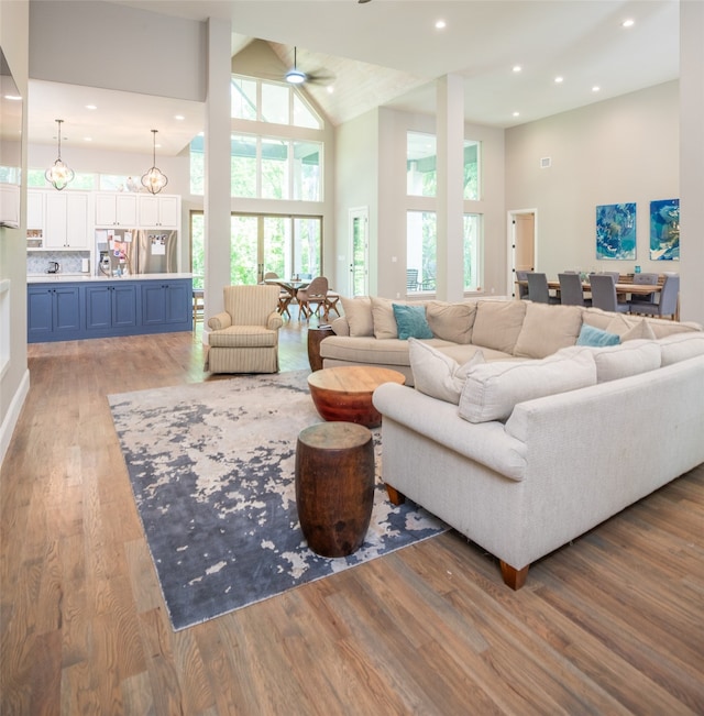 living room with ceiling fan, wood-type flooring, and high vaulted ceiling