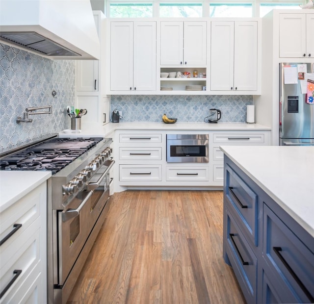 kitchen featuring blue cabinets, white cabinetry, custom range hood, stainless steel appliances, and light hardwood / wood-style floors