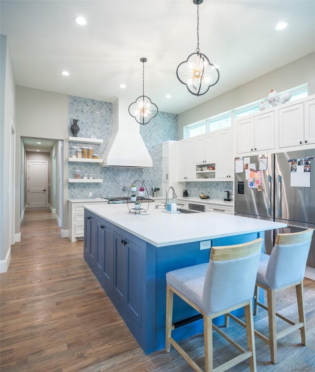 kitchen with a breakfast bar area, custom exhaust hood, white cabinetry, hanging light fixtures, and a kitchen island with sink