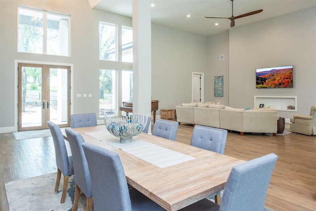 dining area featuring a towering ceiling, light hardwood / wood-style floors, french doors, and ceiling fan