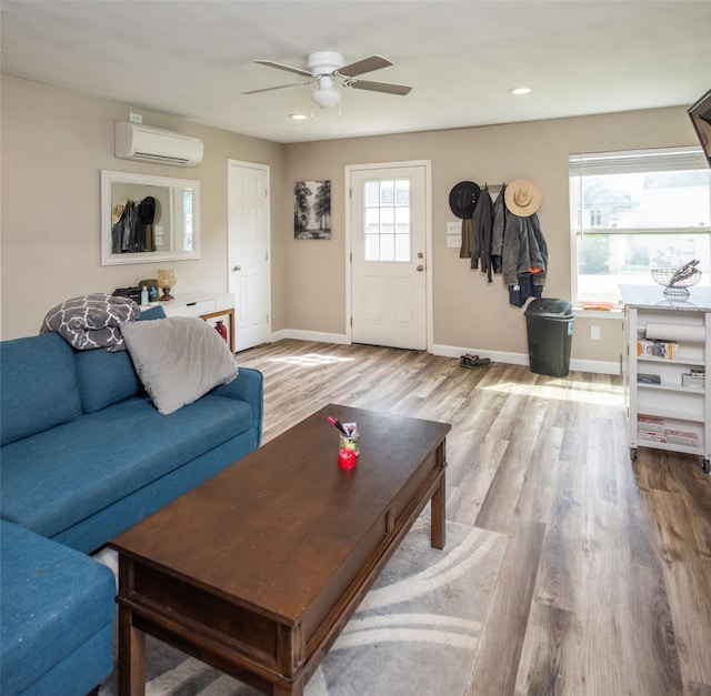 living room with ceiling fan, a wall mounted air conditioner, and light wood-type flooring