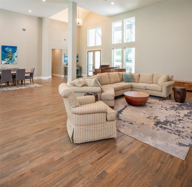 living room with a towering ceiling, a chandelier, and light wood-type flooring