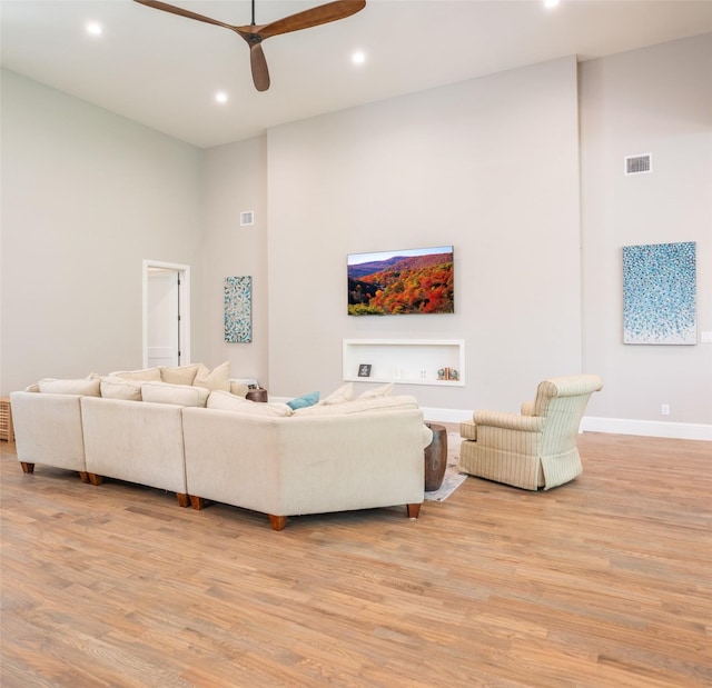 living room with ceiling fan, light hardwood / wood-style flooring, and a high ceiling