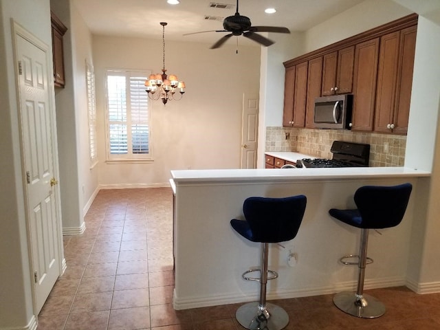 kitchen with a kitchen breakfast bar, stainless steel microwave, black gas stove, decorative backsplash, and brown cabinetry
