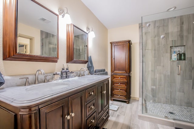 bathroom featuring vanity with extensive cabinet space, double sink, an enclosed shower, and wood-type flooring