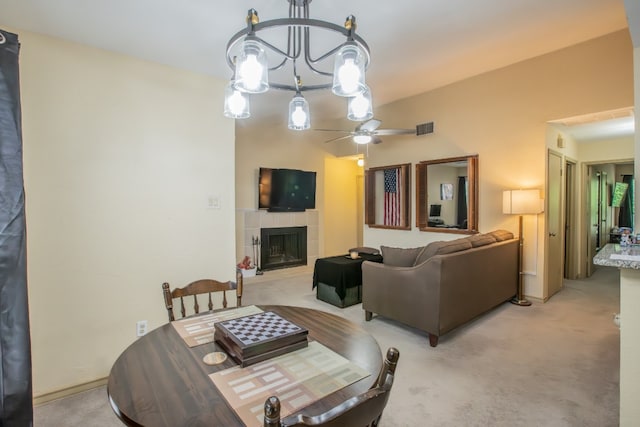 dining area with ceiling fan with notable chandelier, light carpet, and a tile fireplace