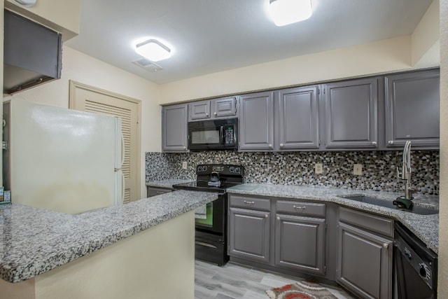 kitchen featuring sink, light hardwood / wood-style floors, tasteful backsplash, gray cabinetry, and black appliances