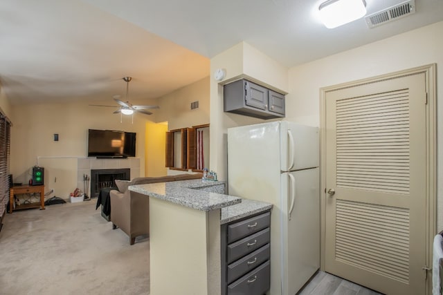 kitchen with a fireplace, white refrigerator, gray cabinetry, light stone counters, and ceiling fan