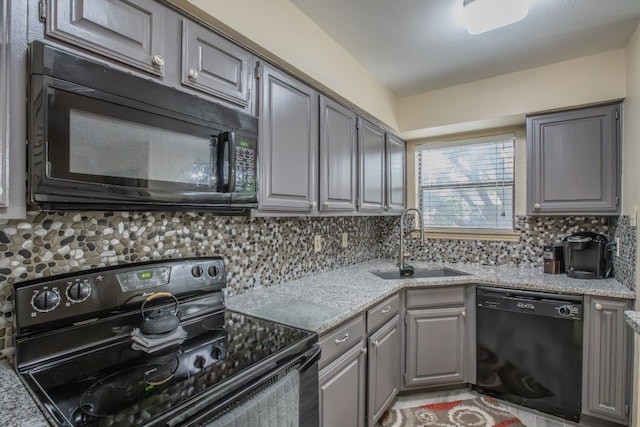 kitchen with light stone countertops, gray cabinetry, black appliances, sink, and tasteful backsplash