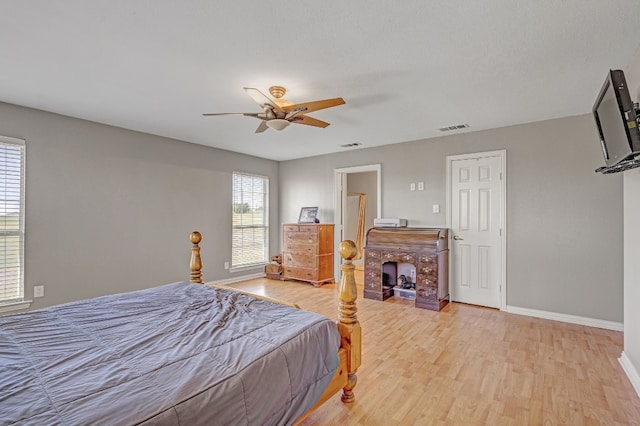 bedroom featuring ceiling fan, light wood-type flooring, and a fireplace