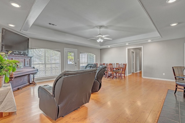 living room with ceiling fan, light wood-type flooring, and a tray ceiling