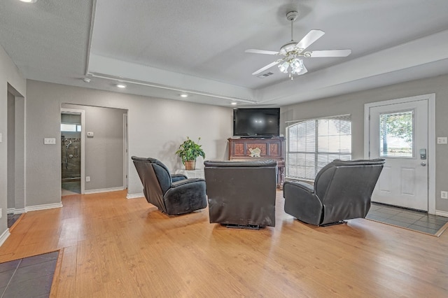 living room featuring light hardwood / wood-style flooring, ceiling fan, and a tray ceiling