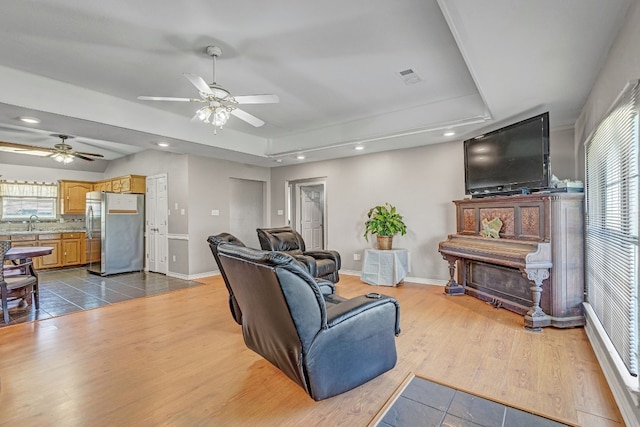 living room with light hardwood / wood-style flooring, ceiling fan, and a raised ceiling