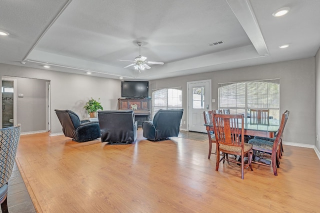 dining area featuring a raised ceiling, ceiling fan, and light hardwood / wood-style floors