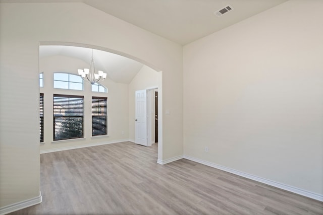 spare room with an inviting chandelier, vaulted ceiling, and light wood-type flooring